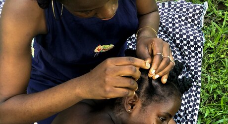 A Black woman braiding another Black woman's natural hair